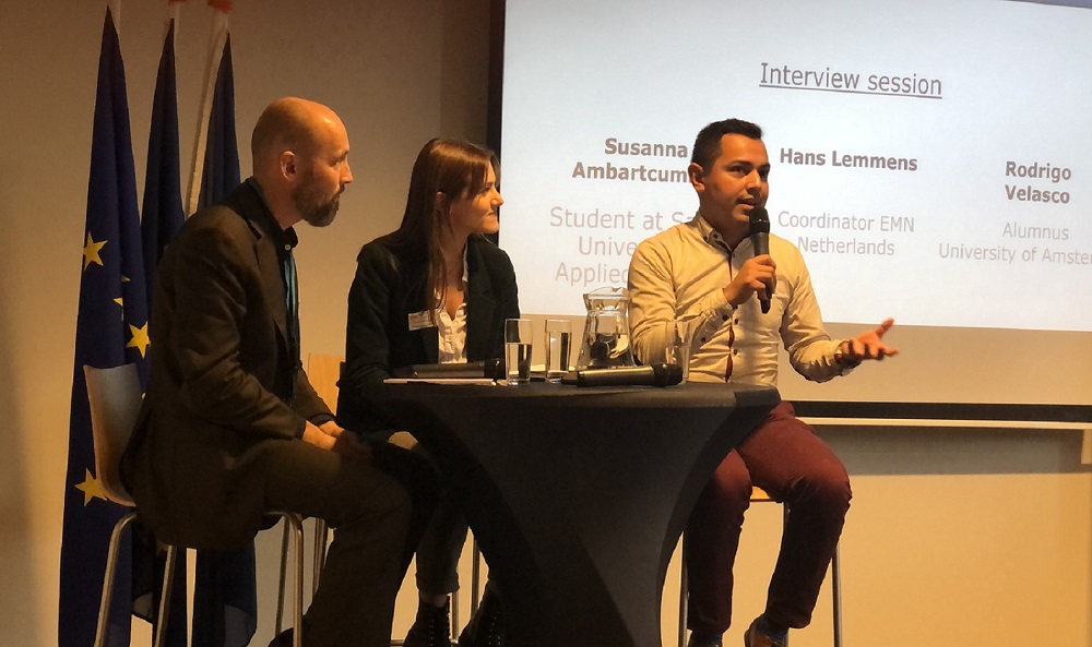 Internationale studenten Rodrigo Velasco (Mexicaans) en Susanna Ambartcumian (Russisch/Armeens) in gesprek met Hans Lemmens, coördinator EMN Nederland