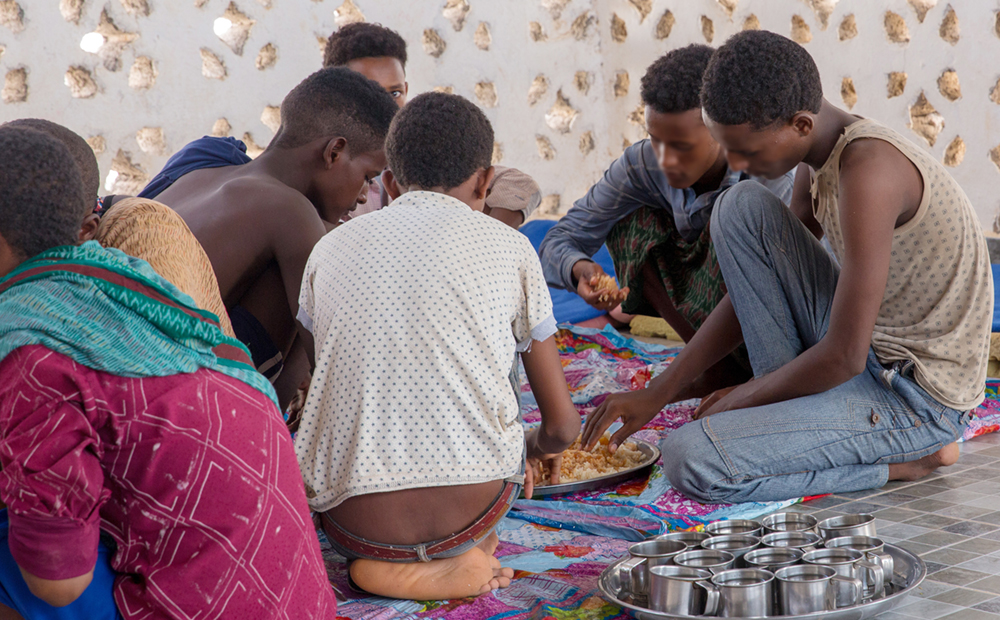 Alleenstaande Somalische jonge migranten eten samen een maaltijd in het Migration Response Center van IOM, waar ze worden verzorgd terwijl ze wachten op hun terugkeer naar huis. IOM voert het traceren van familieleden uit voor niet-begeleide kinderen. Foto: IOM 2018