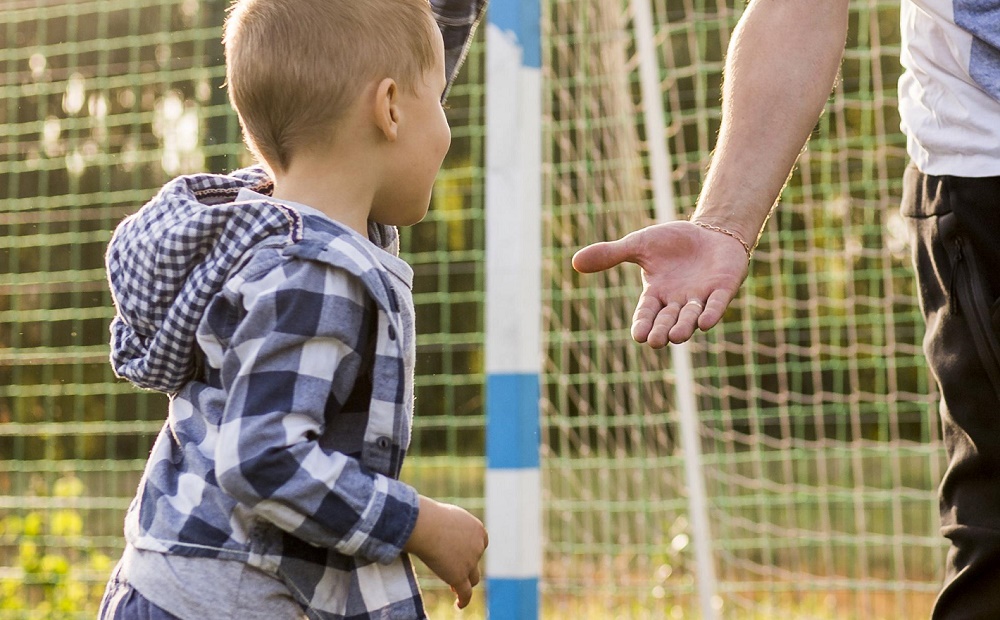 Kind geeft hand aan vader op voetbalveldje